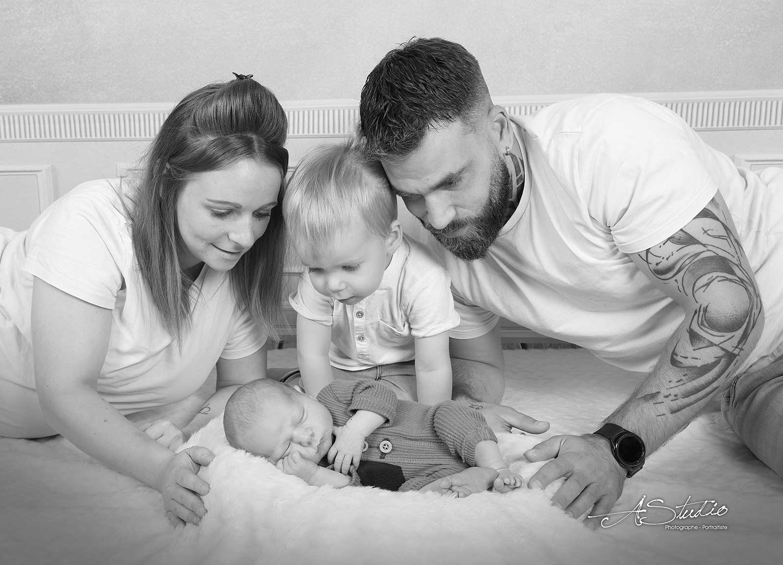 Parents et grand frère autour de leur nouveau-né en noir et blanc